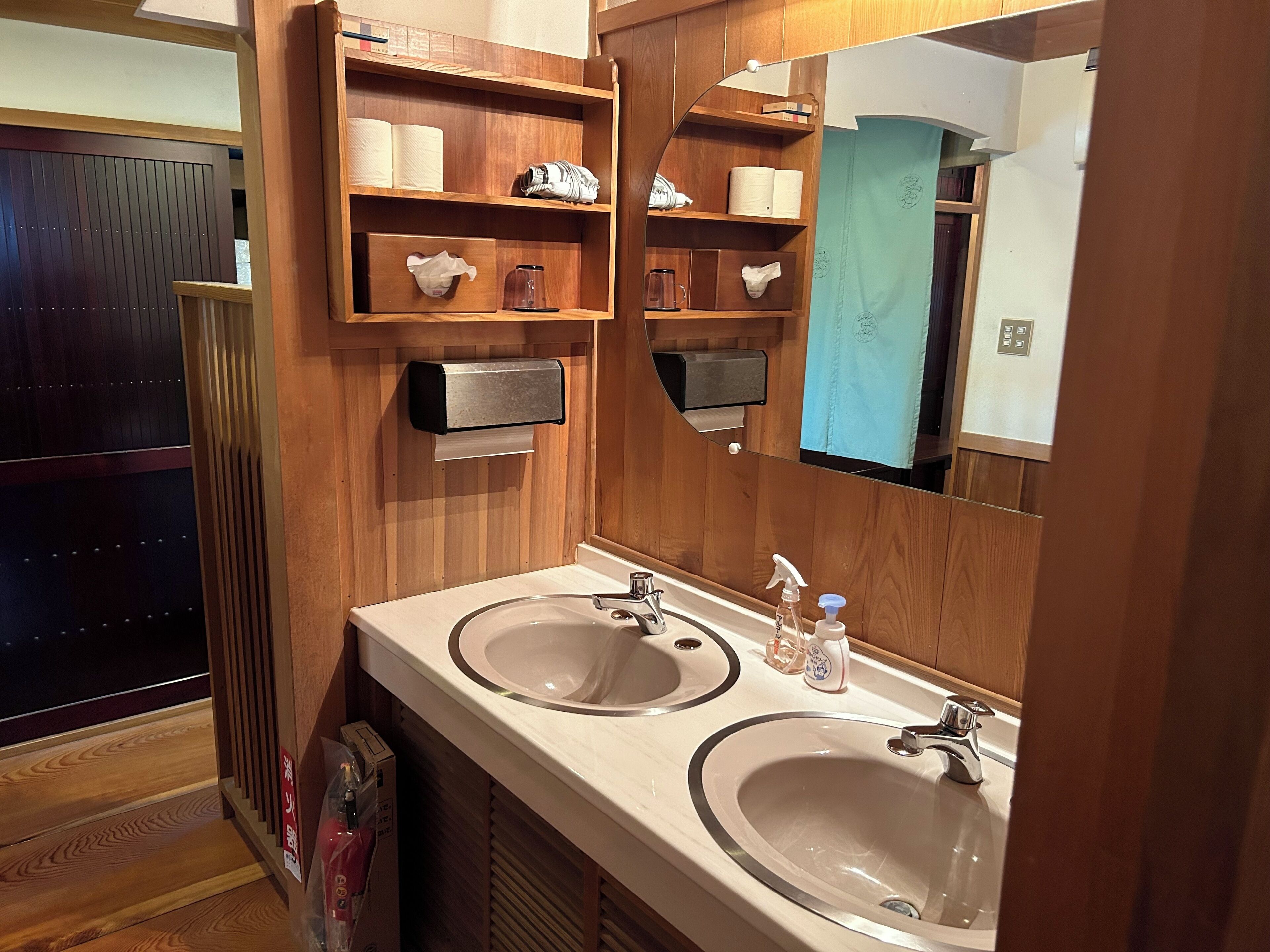 Un baño con paneles de madera, dos lavamanos, un espejo y estantes con artículos de tocador.