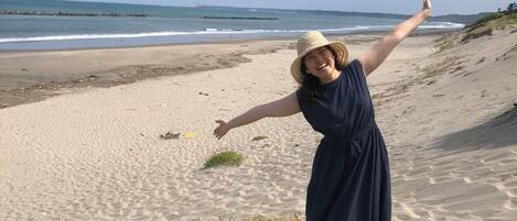 A beach with a person in a blue dress and straw hat.