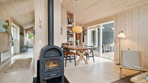 A cozy wooden interior with a central fireplace, a dining area, and a view through a glass door.