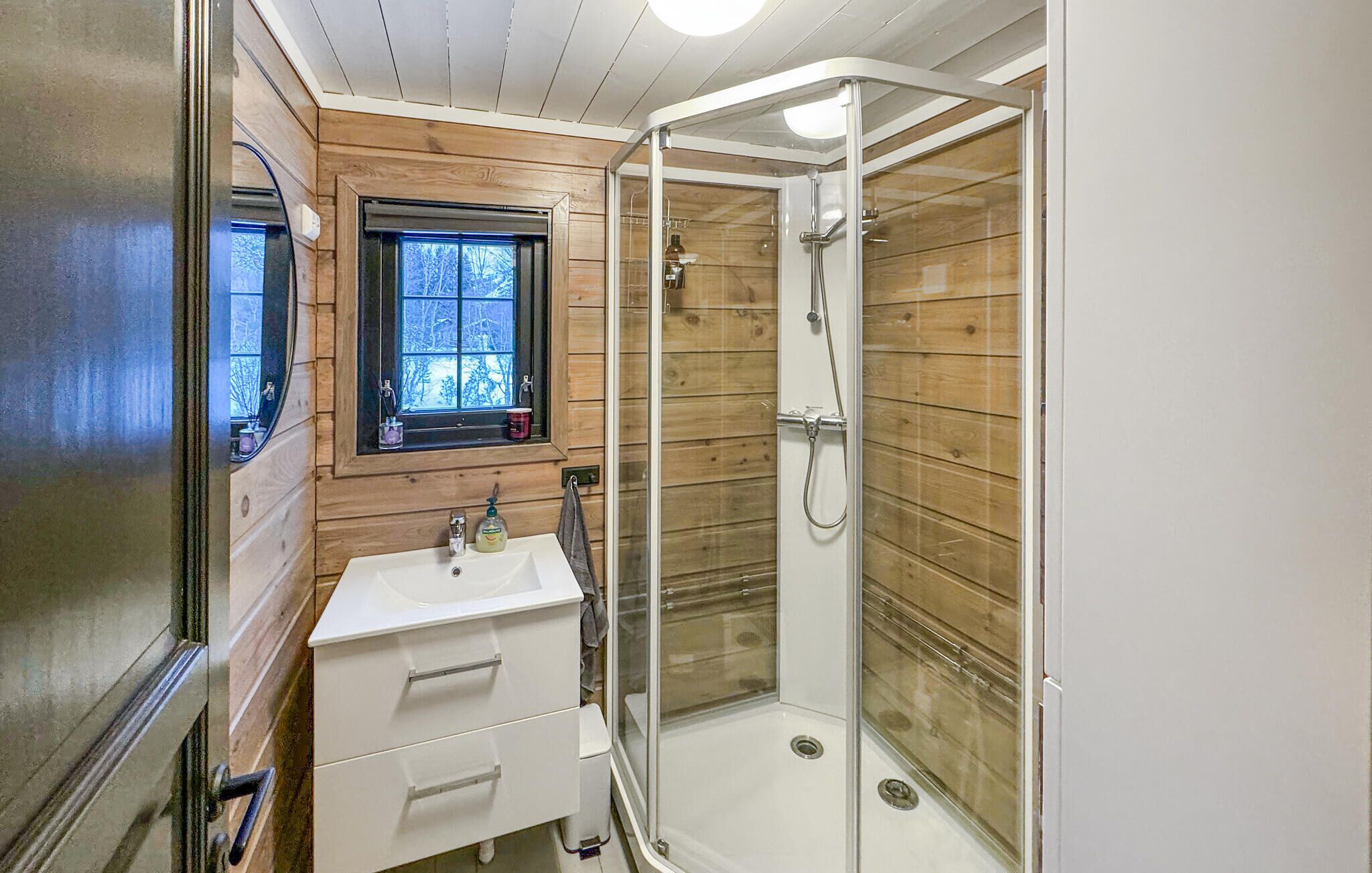 A bathroom with a wooden interior, a window, a sink, and a glass-enclosed shower.