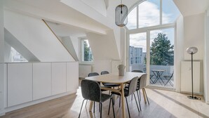 Una cocina moderna con una amplia mesa de comedor, muebles blancos y vistas de la ciudad a través de grandes ventanales.