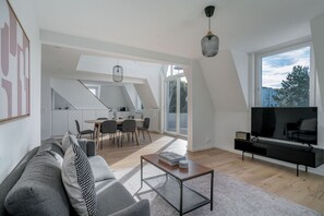 A modern loft apartment with a dining area, a living room with a sofa and TV, and large windows offering a city view. - Delightful Wipkingen 2BR w/ Private W/D, nr Tram, by Blueground (Zurich)