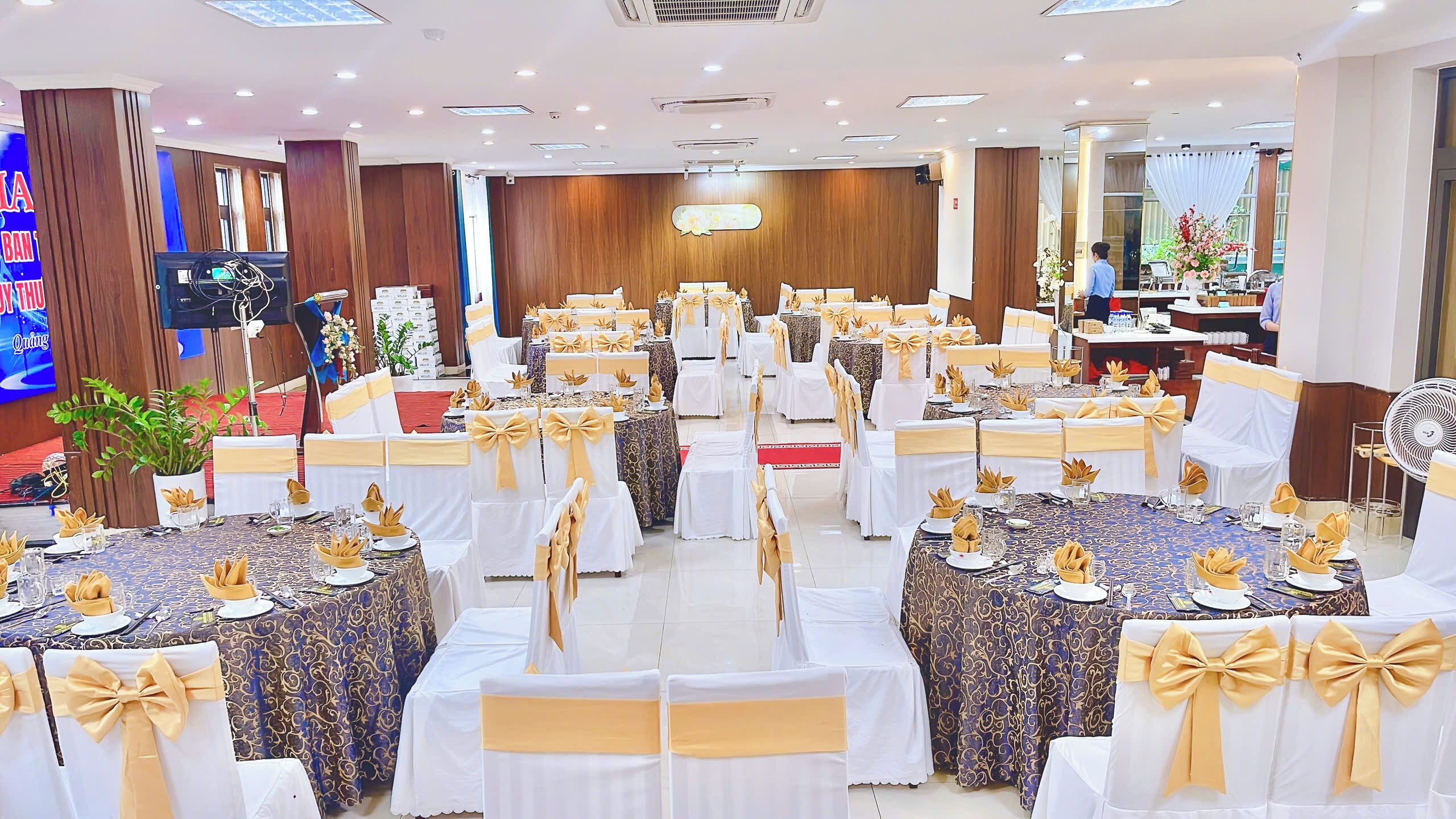A banquet hall with round tables, white chairs, and gold sashes.