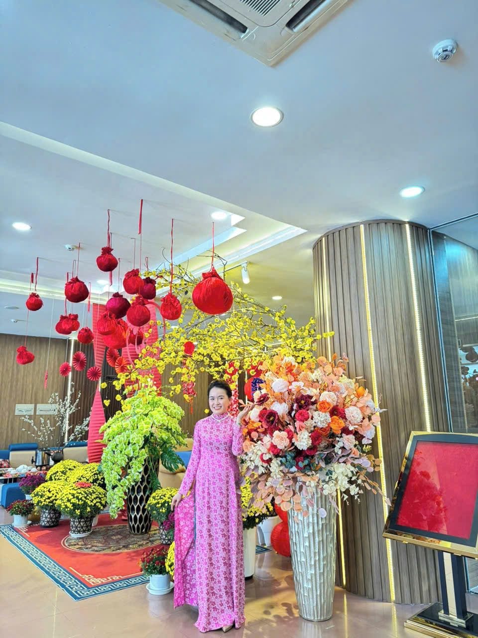 A hotel lobby with a large floral arrangement, a red lantern, and a person in a pink dress.