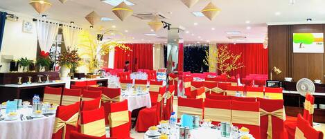 A banquet hall with round tables, red chairs, and gold sashes.