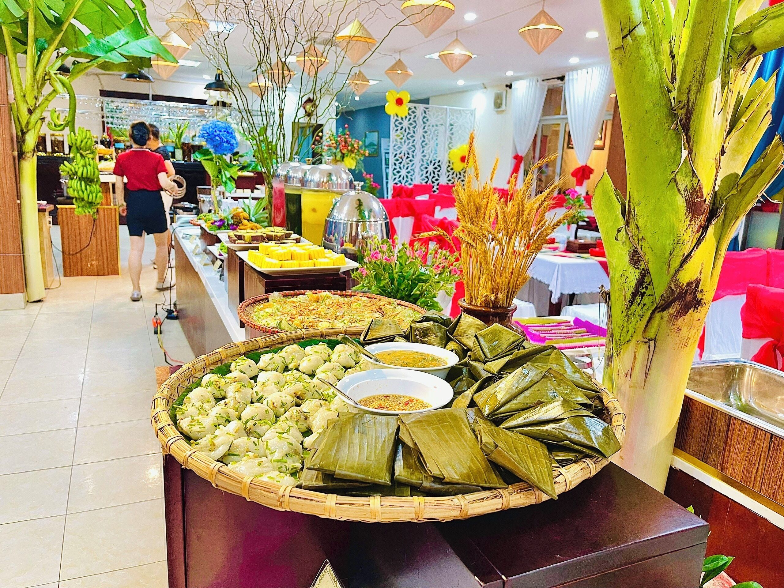 A buffet with various dishes, including rice cakes and wrapped items, in a well-lit indoor setting with a person in the background.