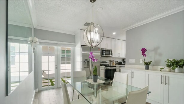 A modern kitchen with white cabinets, a glass dining table, and a chandelier. - Minutes to Palm Beach and Downtown WPB 3 br villa with pool! (West Palm Beach)