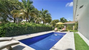 A rectangular swimming pool with a tiled edge, surrounded by a paved deck. There are lounge chairs and a small table with an umbrella. - Minutes to Palm Beach and Downtown WPB 3 br villa with pool! (West Palm Beach)