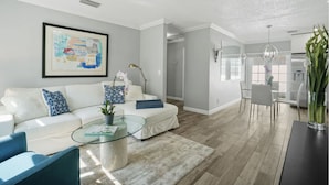 A modern living room with a white sofa, a glass coffee table, and a dining area with a white table and chairs. - Minutes to Palm Beach and Downtown WPB 3 br villa with pool! (West Palm Beach)