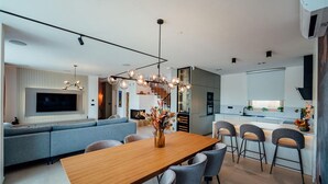 A modern living room with a wooden dining table, grey sofas, and a TV mounted on the wall. - Cozy home in Cista Velika with sauna (Cista Velika)