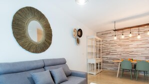 Una sala moderna con un sofá gris, una mesa de centro de vidrio y un comedor con una pared de madera y luces colgantes.