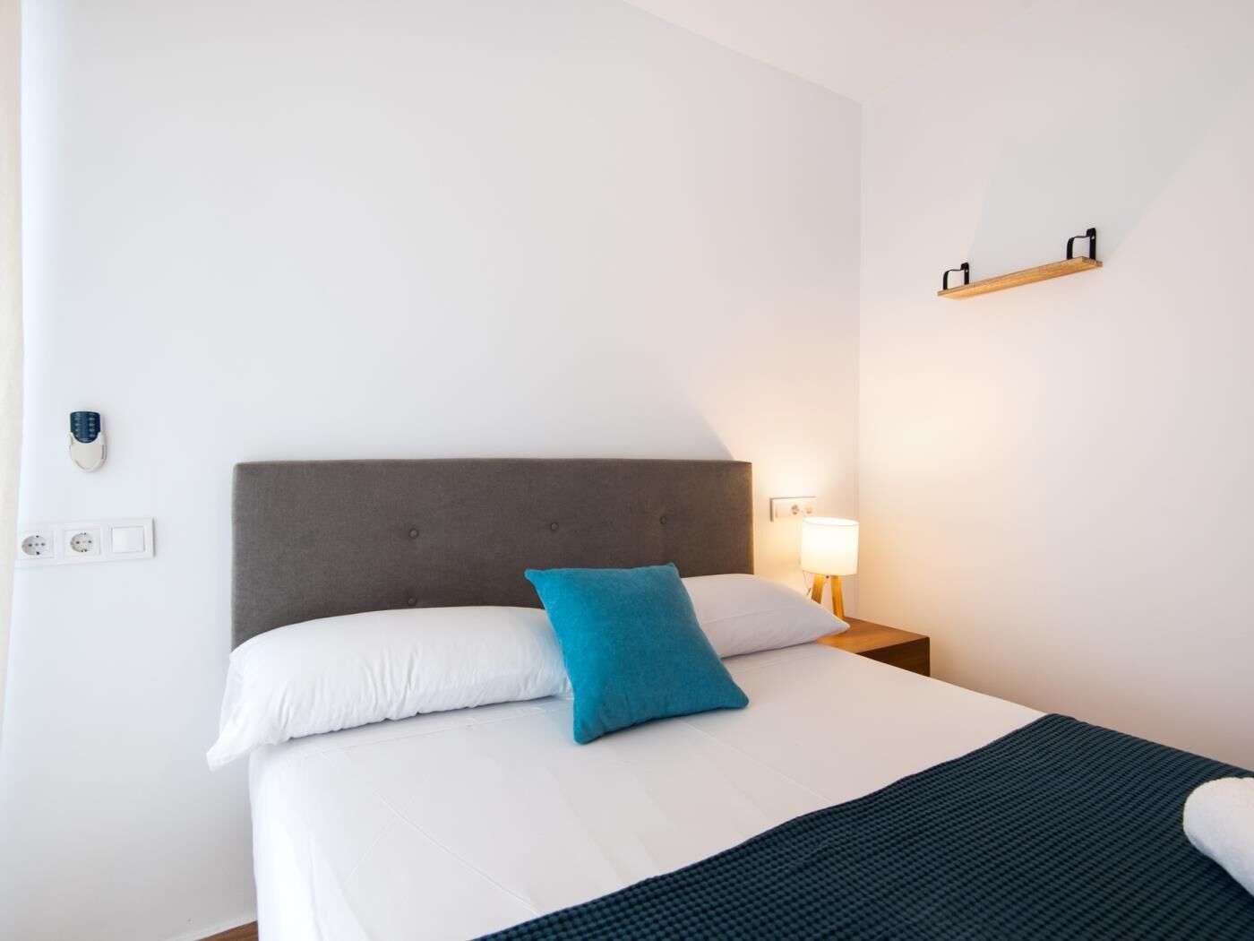 Ein ordentlich bezogenes Bett mit weißer und blauer Bettwäsche, einem grauen Kopfteil und einer Nachttischlampe.