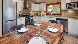 Una cocina moderna con armarios blancos, electrodomésticos de acero inoxidable y una mesa de comedor de madera para cuatro personas.