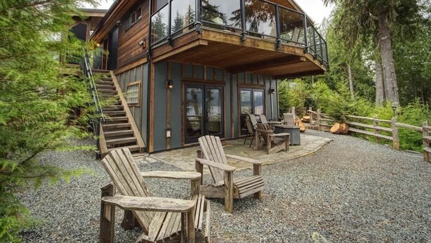 Eine moderne Holzhütte mit Balkon, Sitzgelegenheit im Freien und einem Schotterweg.
