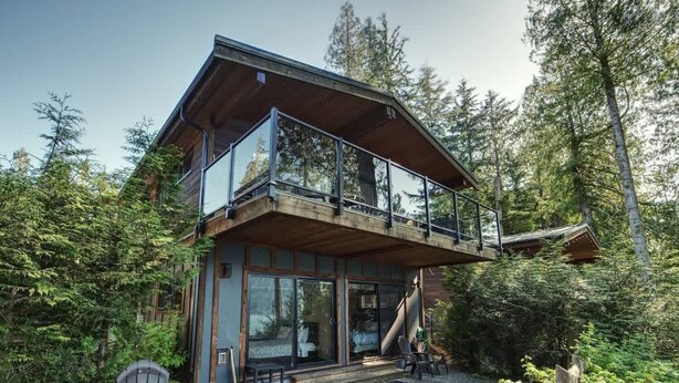 A modern two-story cabin with large glass windows and a wooden deck.