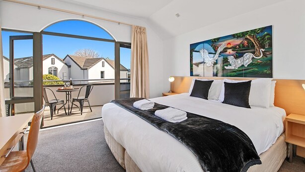 Een hotelkamer met een groot bed, een bureau met stoelen, een balkon met uitzicht op huizen en een schilderij aan de muur.