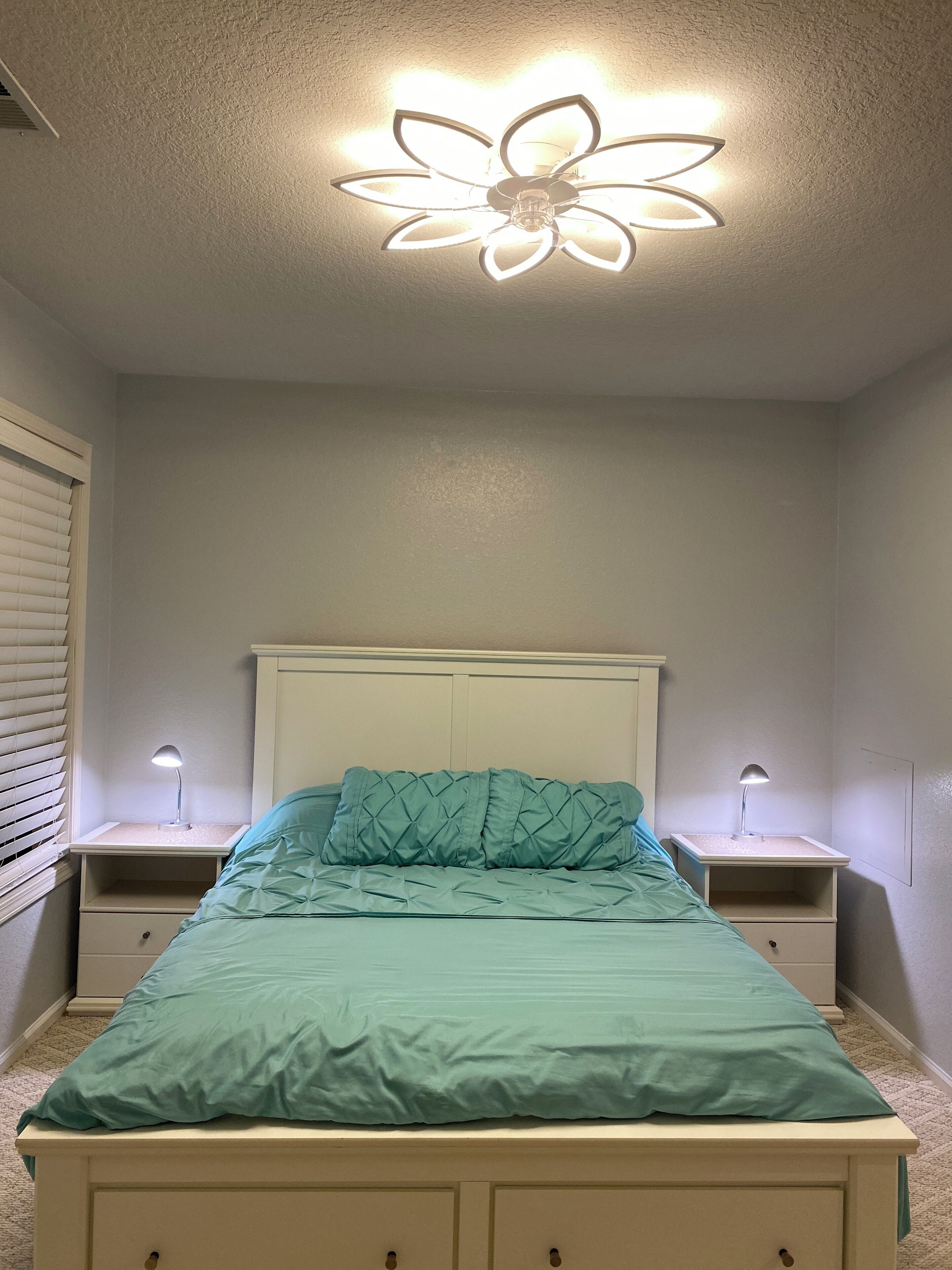 Ein Schlafzimmer mit Bett, zwei Nachttischen, Deckenventilator und einem Fenster mit Jalousien.