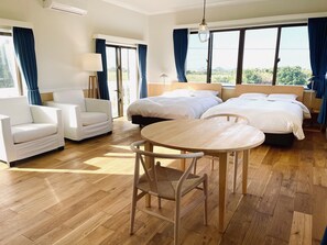 Habitación de hotel con dos camas, una mesa redonda de madera, dos sillones blancos y un gran ventanal con cortinas.