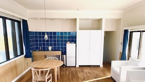 A modern kitchen with a wooden table and chairs, a white refrigerator, and blue-tiled backsplash. - AZZURRA (Miyakojima)