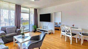 A modern living room with a sofa, a coffee table, a TV, and a dining area with chairs. - Cozy Neuss Apartment with Modern Amenities (Neuss)