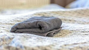 A neatly folded gray towel on a bed with a patterned bedspread. - Cozy Neuss Apartment with Modern Amenities (Neuss)