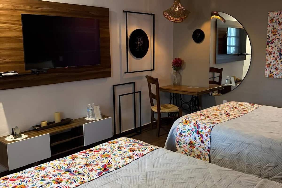 A hotel room with two beds, a desk, a chair, a TV, and a mirror.