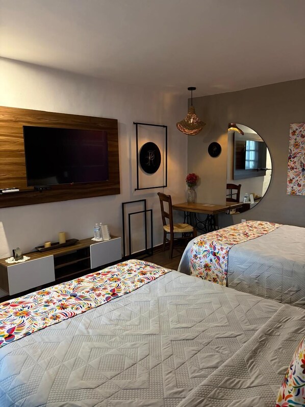 A hotel room with two beds, a desk, a chair, a TV, and a mirror. - Paseo Real Hotel Boutique (Uruapan)