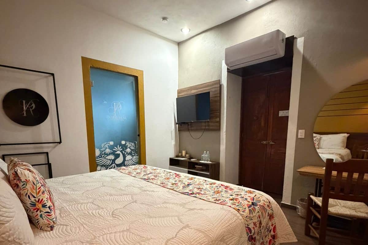 A bedroom with a large bed, a TV mounted on the wall, a wooden door, and a small table.
