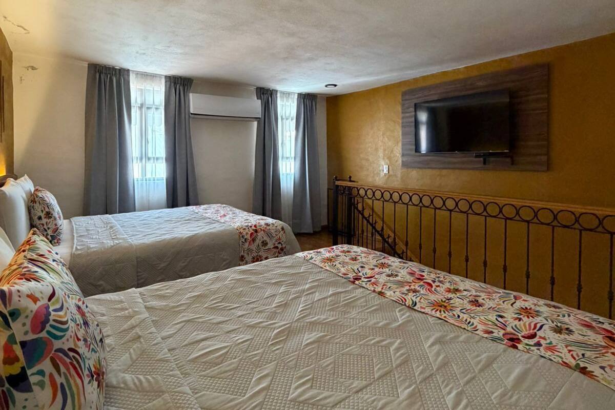 A hotel room with two beds, a television on the wall, and a window with curtains.