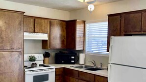 Une cuisine avec des meubles de rangement en bois, une cuisinière blanche, un four à micro-ondes, un évier et un ventilateur de plafond.