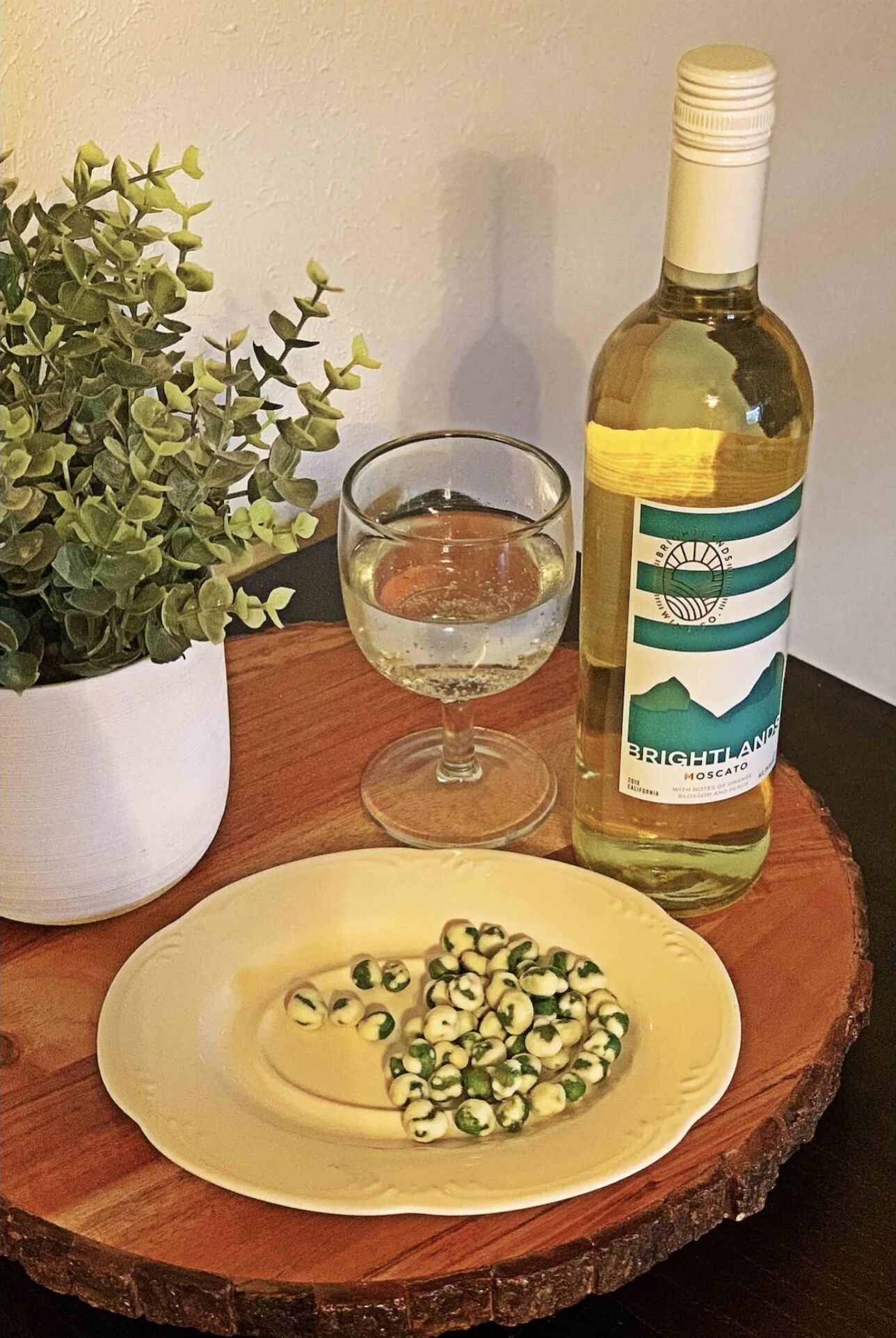A bottle of Brightlands Moscato wine, a glass of water, and a plate with green and white grapes on a wooden table.