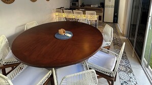 A dining area with a round table surrounded by white wicker chairs with blue cushions, a ceiling fan, and a kitchen in the background. - Casa Colonial en el Centro de Mérida, Remodelada, Excelente Para Grupos Grandes (Centro)