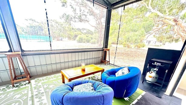 Ein Zimmer mit einem großen Fenster, zwei blauen Sitzsäcken, einem Holztisch mit Kerze und einem Gaskochfeld.