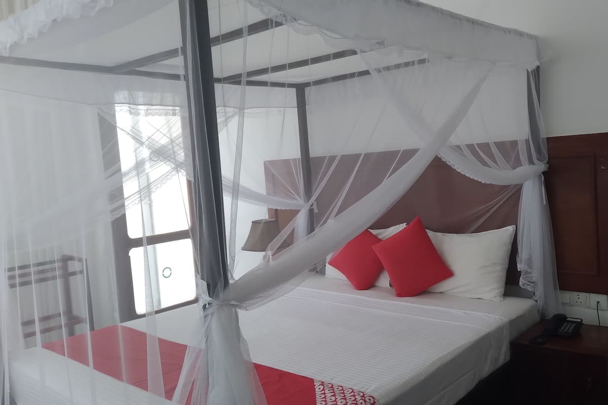A bed with a canopy, a bedside table with a phone, and a wall-mounted light switch.