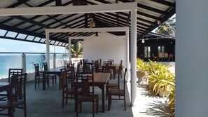 An outdoor dining area with wooden tables and chairs, a white pergola, and a view of the ocean. - Sea Breeze Hotel Ambalangoda (Madampagama)