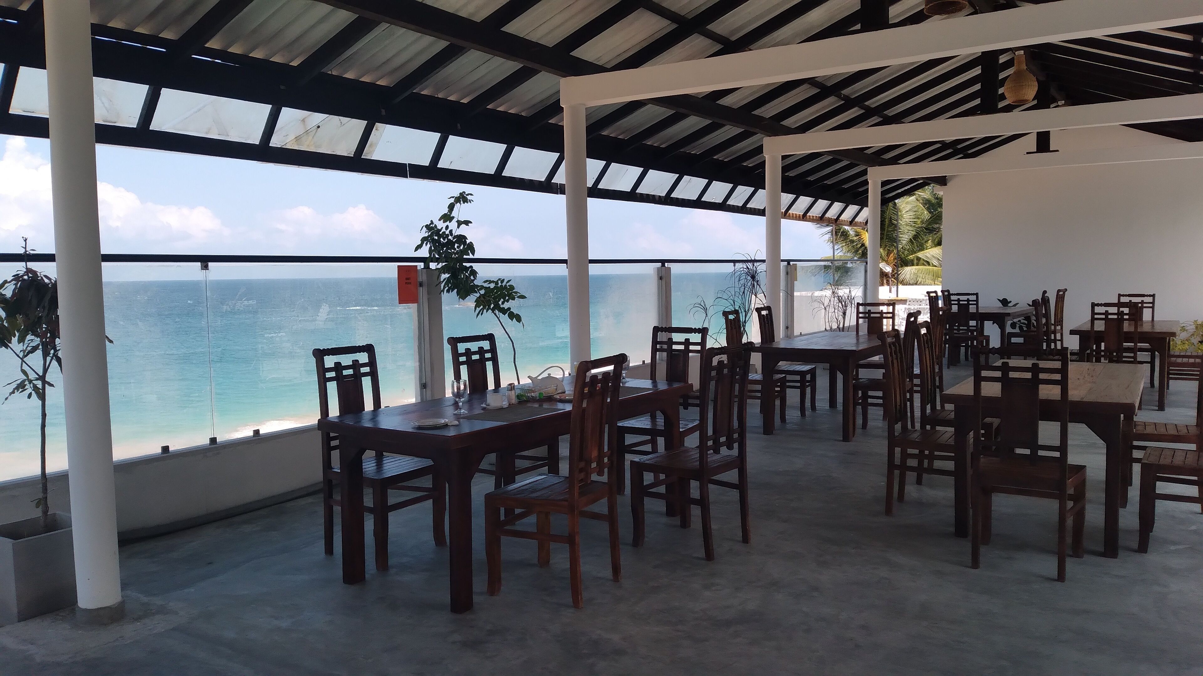 Un espace extérieur abrité, aménagé avec des tables et des chaises, et offrant une vue sur la plage.
