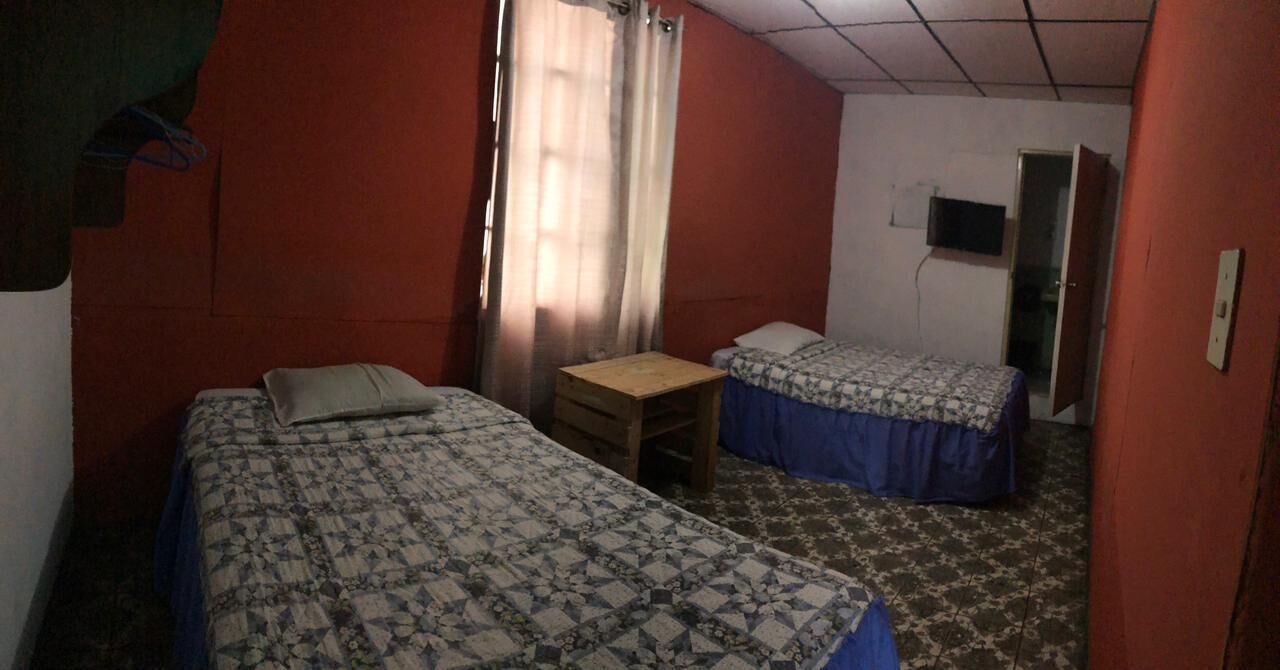 A room with two beds, a small table, and a television on the wall.