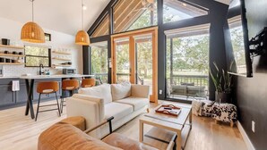 A modern interior with a kitchen, dining area, and living room. There are large windows, a sofa, and a coffee table.