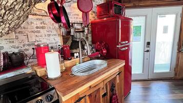A rustic kitchen with a wooden island, a stove, and a red refrigerator.