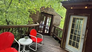 Une terrasse en bois avec des chaises rouges et une petite table, entourée d’arbres verdoyants.