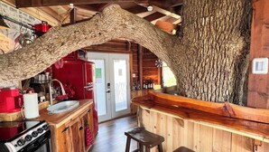 Une cuisine rustique avec un plafond en bois, un grand tronc d’arbre intégré à la décoration, un réfrigérateur rouge et une cuisinière.