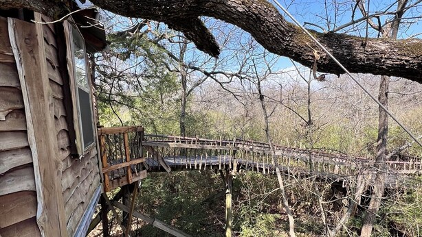Une cabane en bois dotée d’une terrasse et d’un pont menant à une zone boisée.