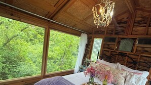 Une chambre dans une cabane en bois, avec un grand lit, un lustre et une vue sur la verdure environnante.