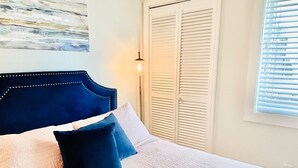 A bedroom with a bed, pillows, a headboard, a nightstand, a wall-mounted lamp, a window with blinds, and a door with louvered shutters. - Riley's Retreat - Resort Pool/HotTub/Ski/Sled/Tube (Beech Mountain)