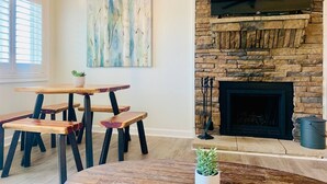 A dining area with a stone fireplace, a flat-screen TV mounted above it, and a painting on the wall. - Riley's Retreat - Resort Pool/HotTub/Ski/Sled/Tube (Beech Mountain)