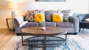 A living room with a grey sofa, yellow cushions, a round coffee table, and a painting on the wall. - Riley's Retreat - Resort Pool/HotTub/Ski/Sled/Tube (Beech Mountain)