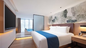 A modern hotel room with a large bed, a flat-screen TV, a desk with a phone, and a view of the city through large windows. - NAIVE L Executive Apartments Coast City (Shenzhen)