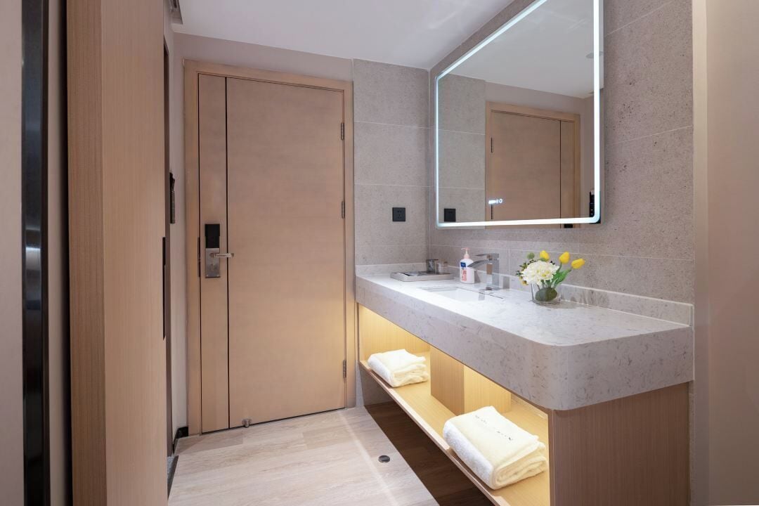 A modern bathroom with a large mirror, two sinks, and a shelf with towels.