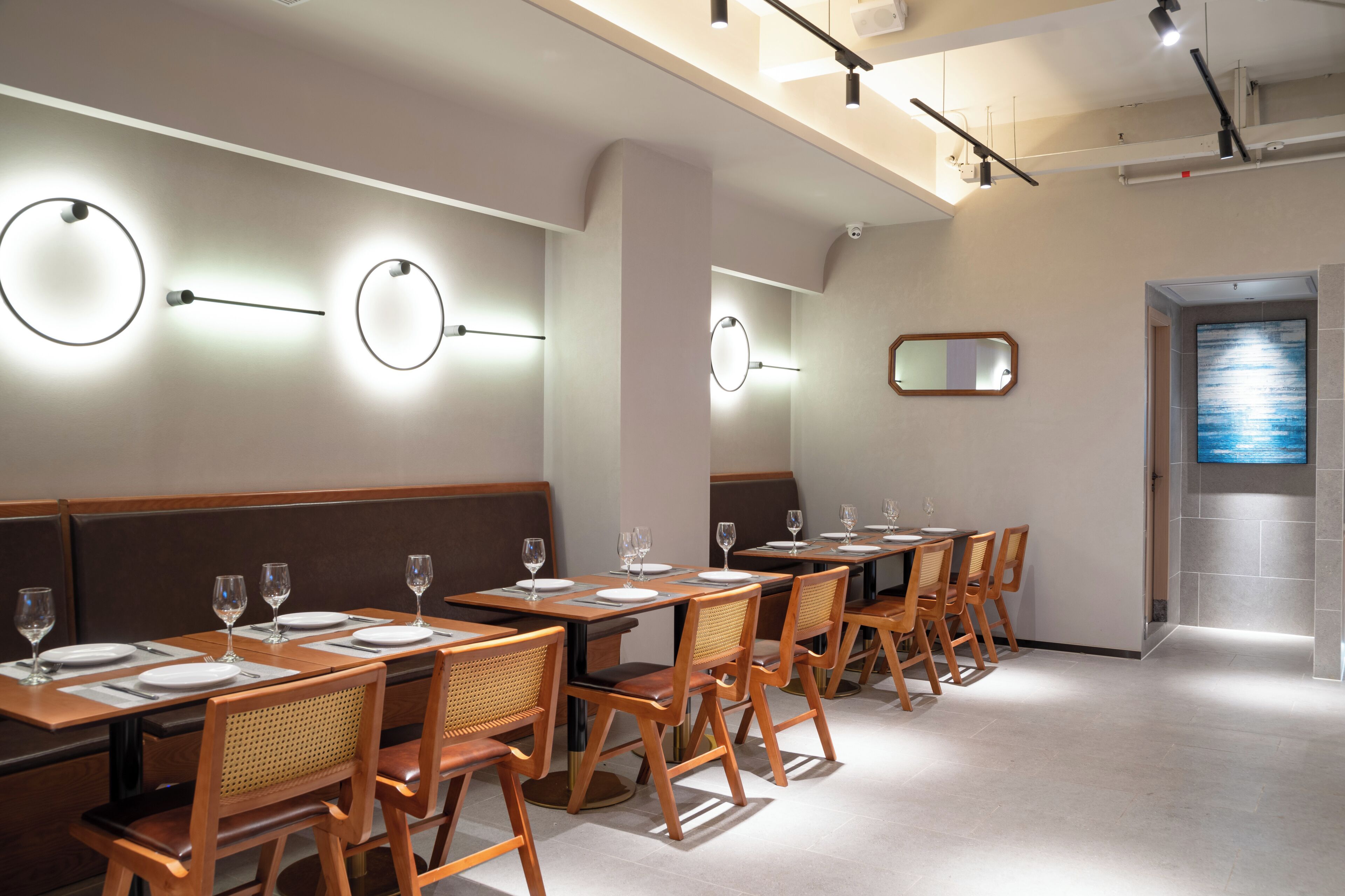 Un restaurante con mesas y sillas de madera, apliques redondos en la pared y un espejo grande.