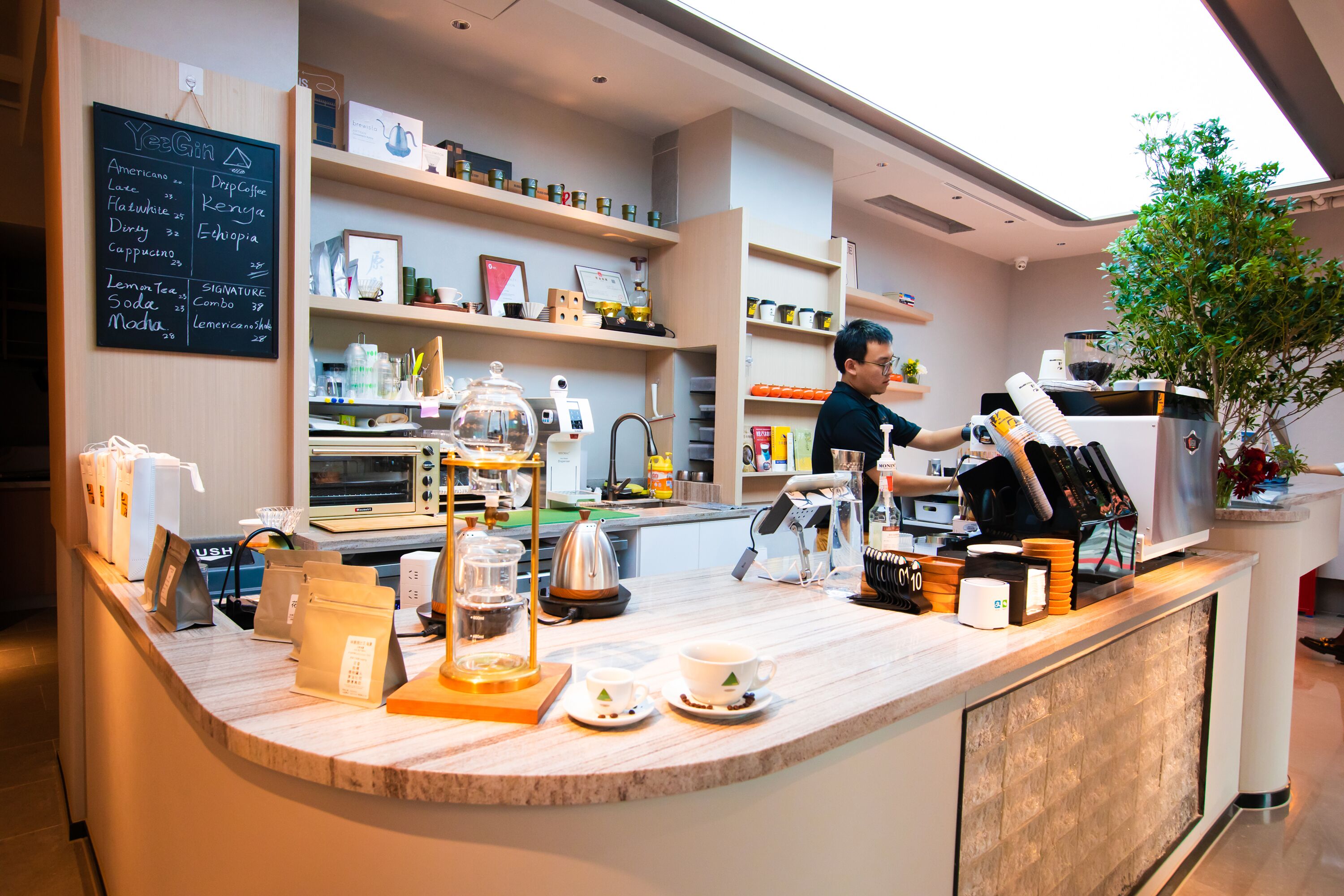 Una cafetería moderna con mostrador, estantes con diversos productos y un menú en la pared.